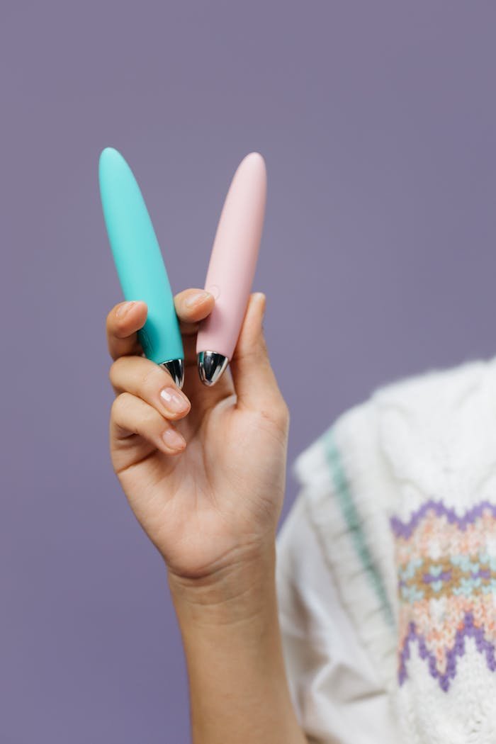 Close-up of a hand holding pink and blue vibrators against a purple background.